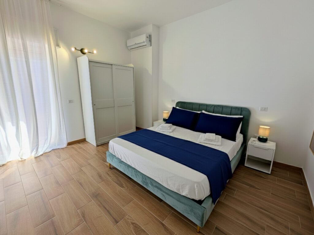 Letto matrimoniale con testiera in velluto verde e armadio bianco nella Camera Porta Napoli, B&B a Lecce