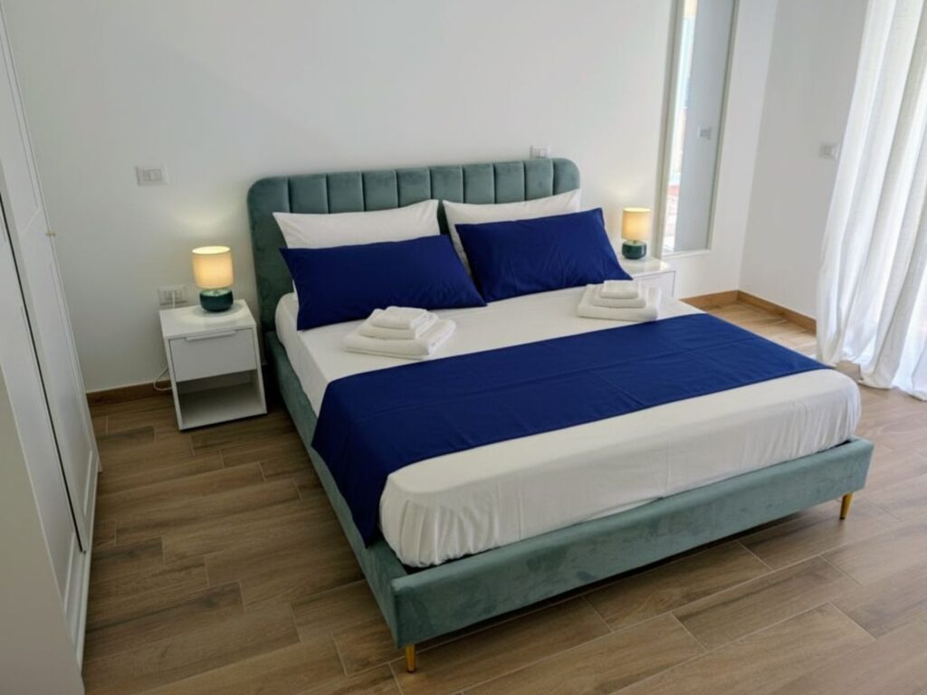 Letto matrimoniale con testiera in velluto verde e biancheria blu in camera del B&B a Lecce